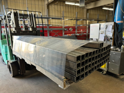 Pallet load of long, metal parts on a forklift shown stretch wrapped by the TAB Wrapper Tornado orbital wrapper